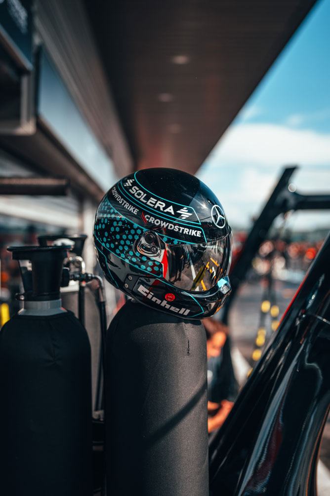 A Mercedes-AMG PETRONAS Formula One Team helmet with prominent sponsor logos including Einhell, CrowdStrike, and Solera is placed on a gas bottle in the pit lane. The reflection on the visor shows the surroundings of the garage.