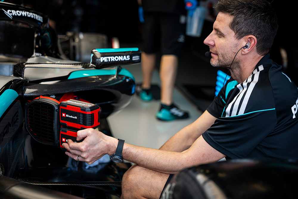 Formula 1 mechanic holding an Einhell battery while working on a race car in the garage.