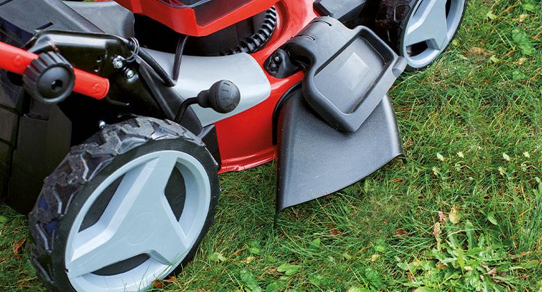 Close-up of the side discharge flap of a red cordless lawn mower while mowing grass.